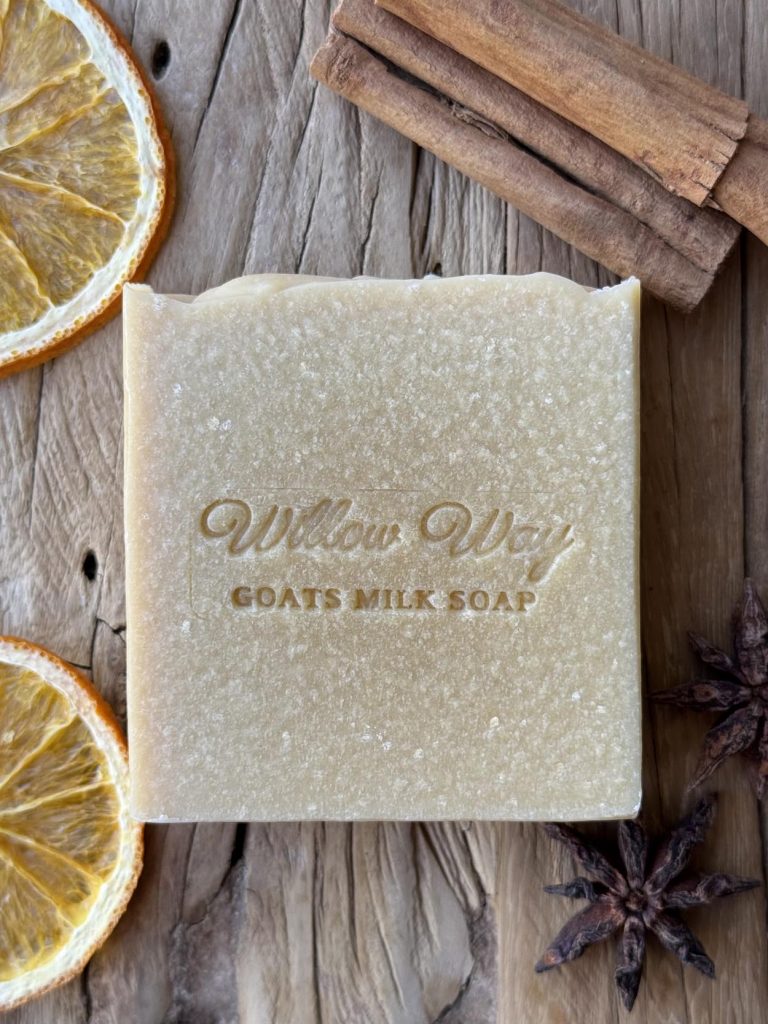 A bar of goats milk soap on a wooden board with orange cinnamon and chai spice
