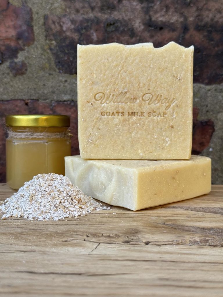 A bar of goats milk soap on a wooden board with a jar of honey and oats
