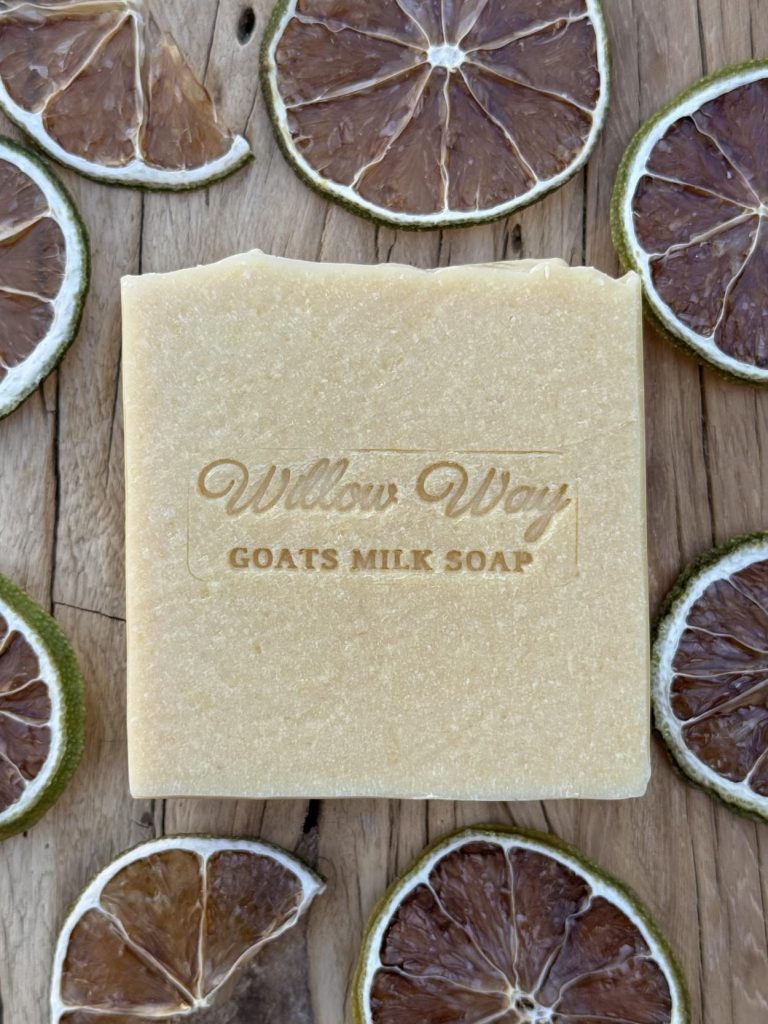 A bar of goats milk soap on a wooden board with slices of patchouli and lime