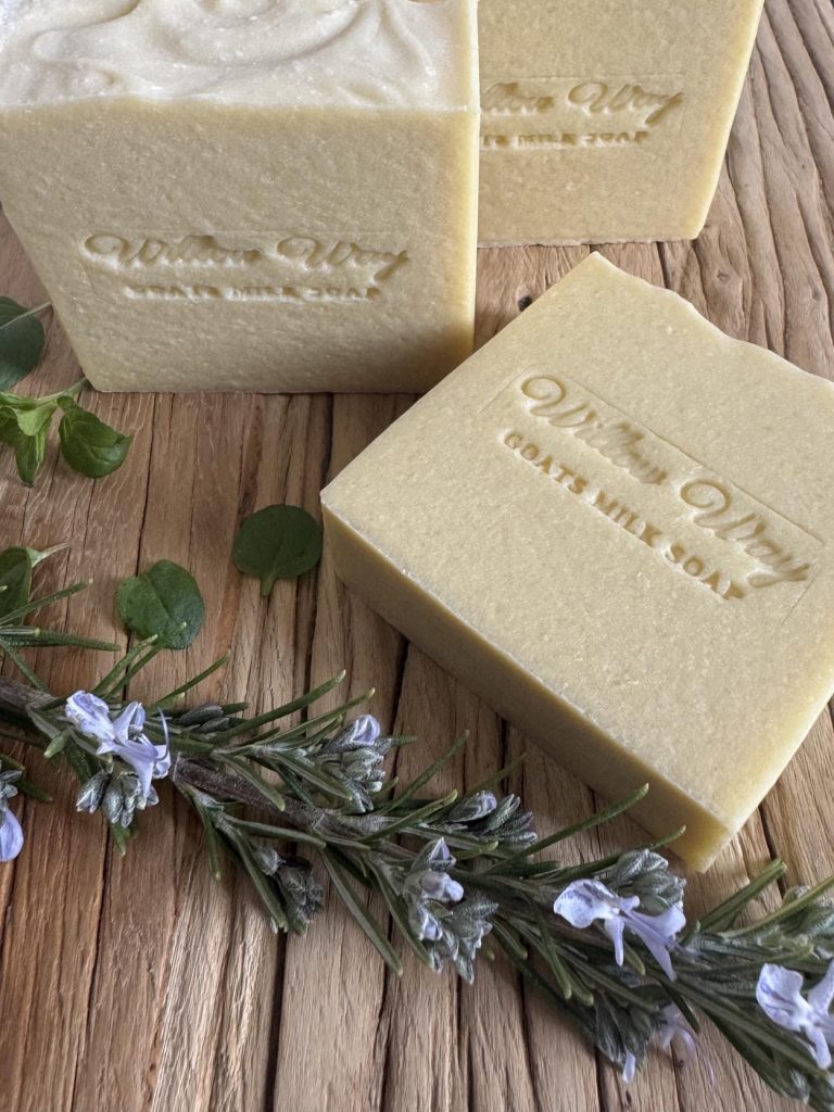 A bar of goats milk soap on a wooden board with rosemary and peppermint